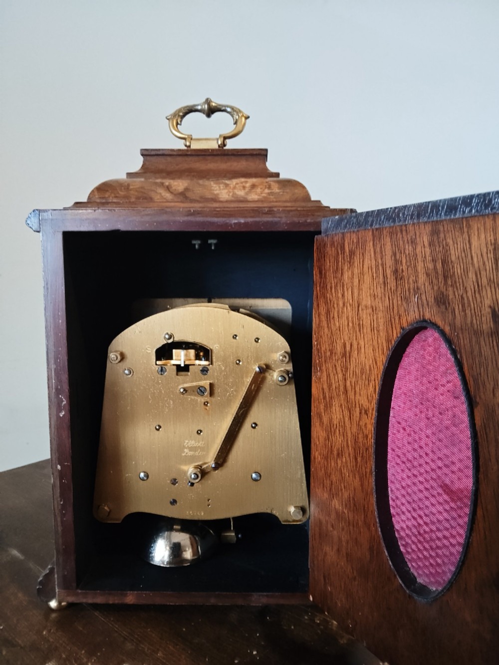A rectangular burr walnut bracket clock featuring a top brass handle, arched brass dial face with Roman numerals, and a silvered chapter ring. View IV
