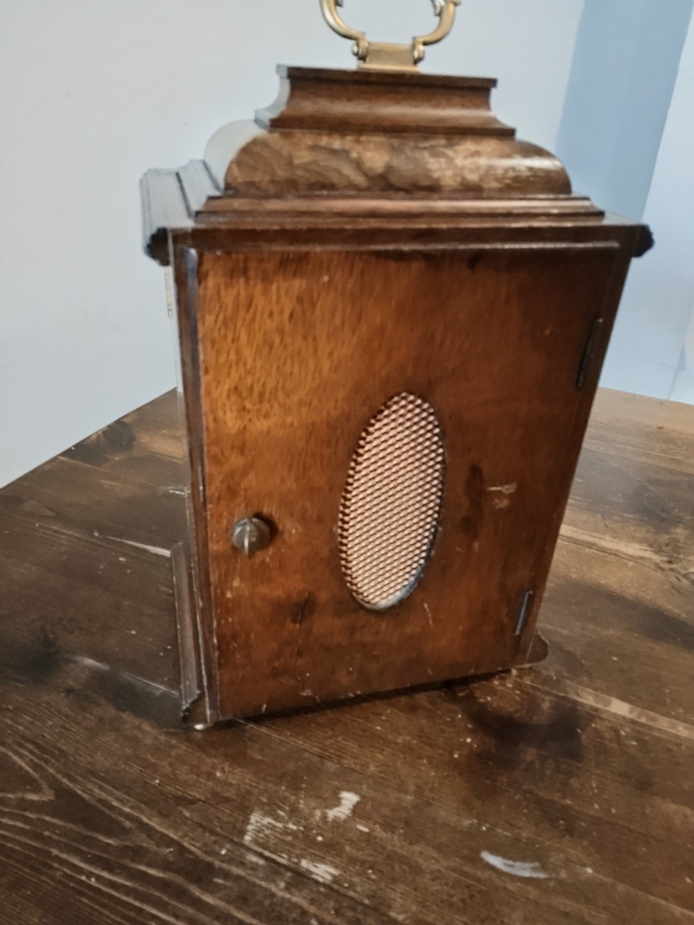 A rectangular burr walnut bracket clock featuring a top brass handle, arched brass dial face with Roman numerals, and a silvered chapter ring. View V