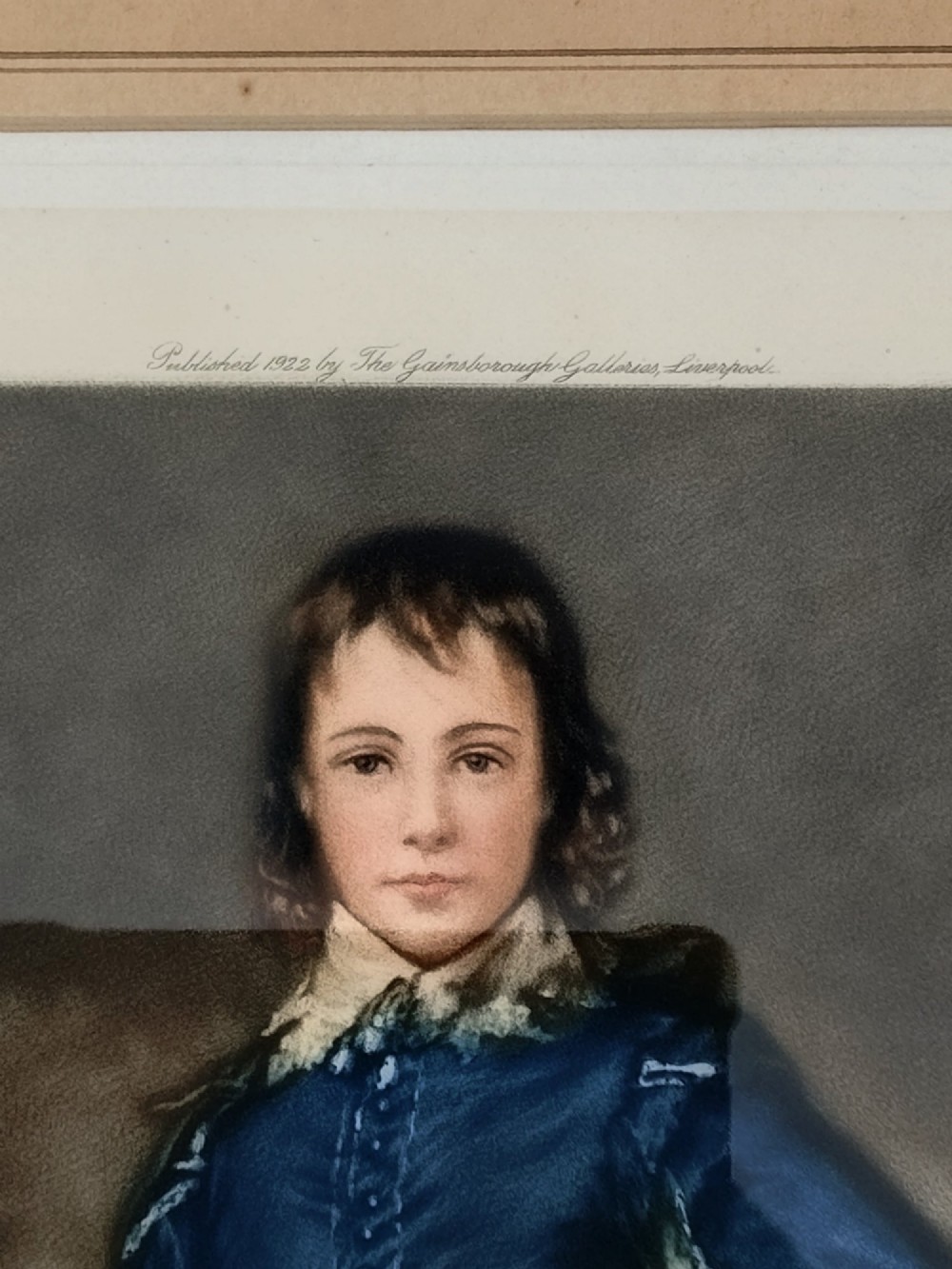 A framed colour portrait print of Thomas Gainsboroughs The Blue Boy, set within a wide beige mount and a gold giltwood frame topped with a bow cresting. View IV