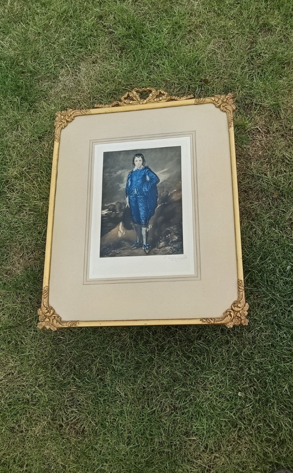 A framed colour portrait print of Thomas Gainsboroughs The Blue Boy, set within a wide beige mount and a gold giltwood frame topped with a bow cresting. View XI