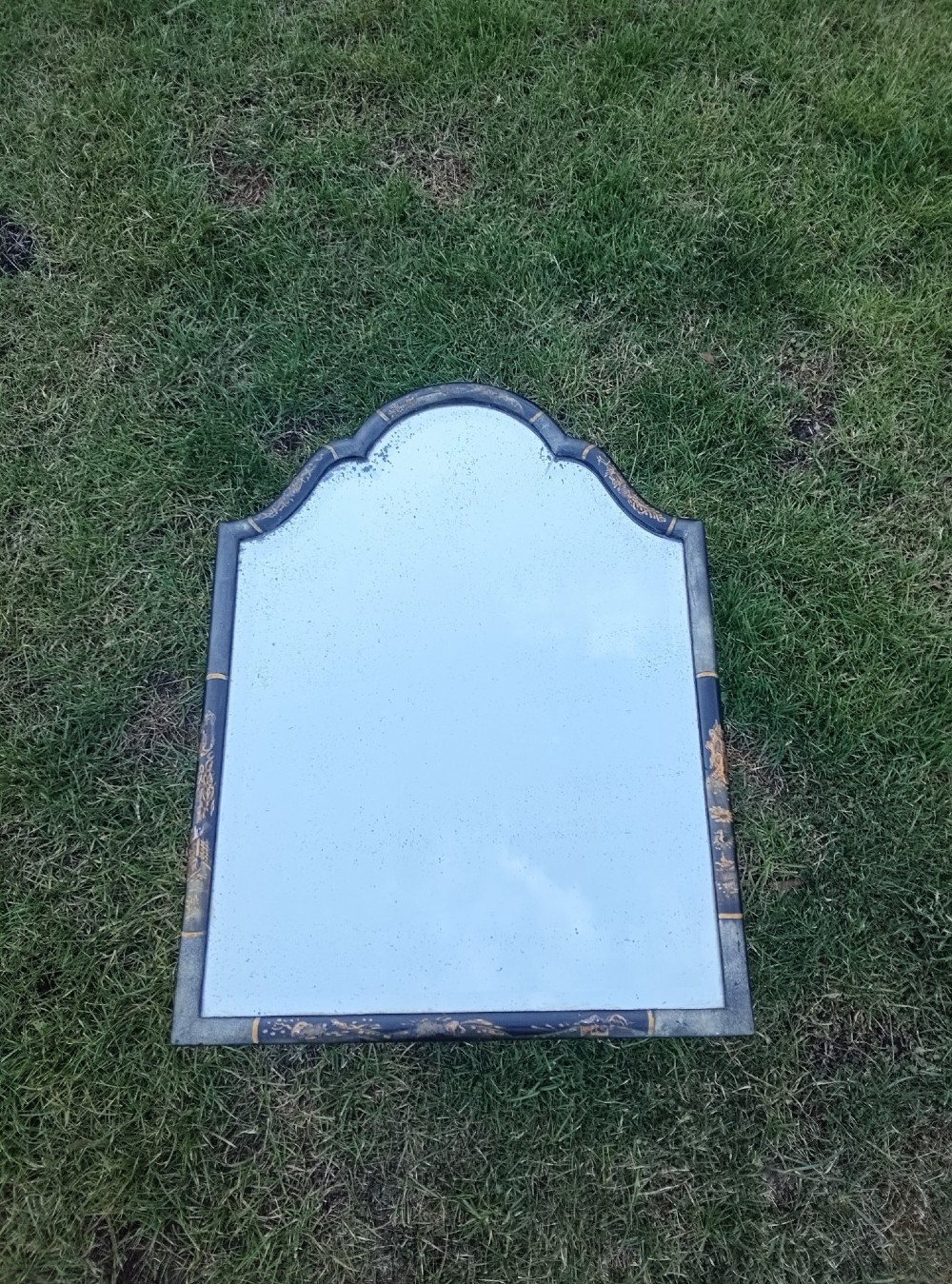 A 19th-century shaped wall mirror featuring a black lacquered frame with hand-painted gold Chinoiserie motifs and a bevelled mirror plate.