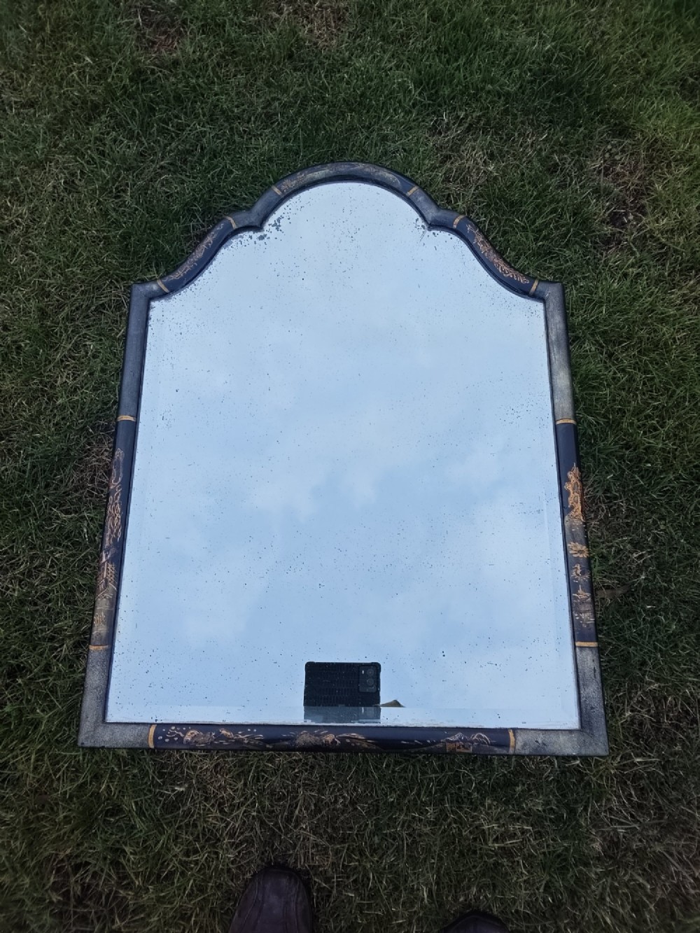 A 19th-century shaped wall mirror featuring a black lacquered frame with hand-painted gold Chinoiserie motifs and a bevelled mirror plate. View X