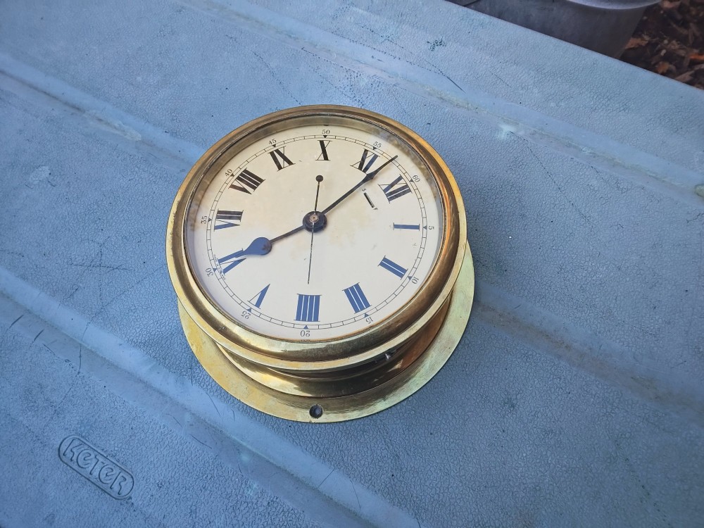 A circular heavy brass marine wall clock featuring a cream dial with black Roman numerals and a flange for wall mounting. View II