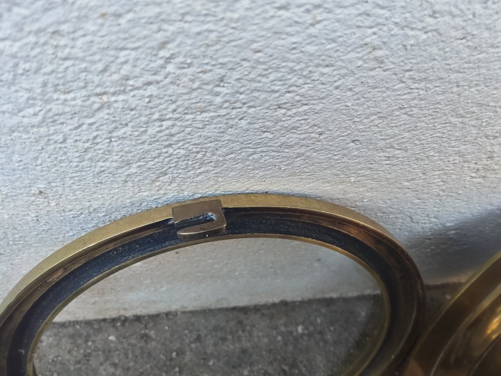 A circular heavy brass marine wall clock featuring a cream dial with black Roman numerals and a flange for wall mounting. View VII