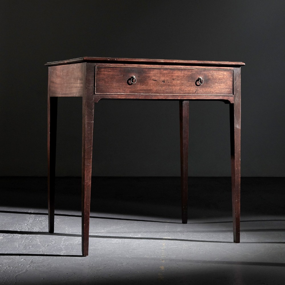 A George II mahogany side table featuring a single drawer with two small brass ring handles, raised on straight tapered legs.