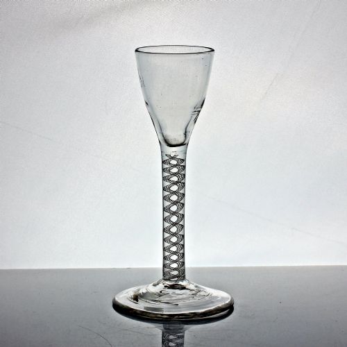 fig 1. An antique clear glass wine glass featuring a bell-shaped bowl, an internal white opaque twist stem, and a flat conical base.