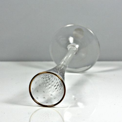 fig 2. A tall Georgian clear lead glass ratafia flute featuring an engraved star pattern, gilded rim, white double series opaque twist stem, and a flat circular foot.