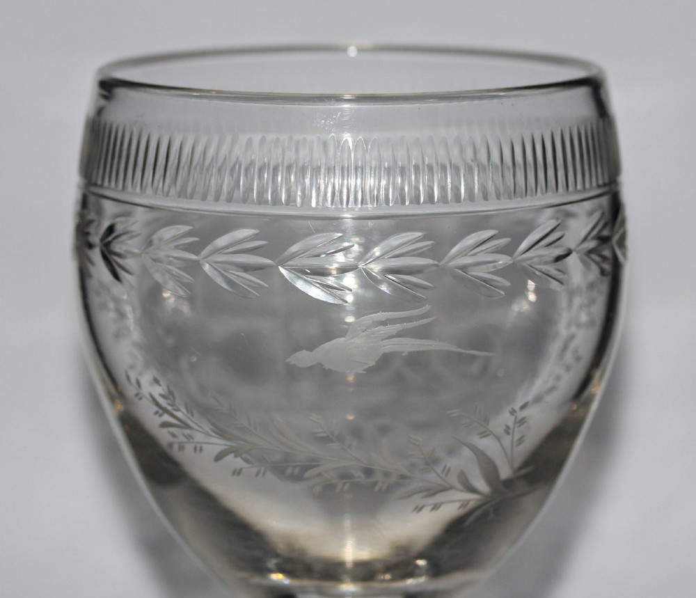 A clear Georgian glass goblet featuring an ovoid bowl with a wheel-engraved monogram and floral wreath above a short plain stem and circular foot. View V