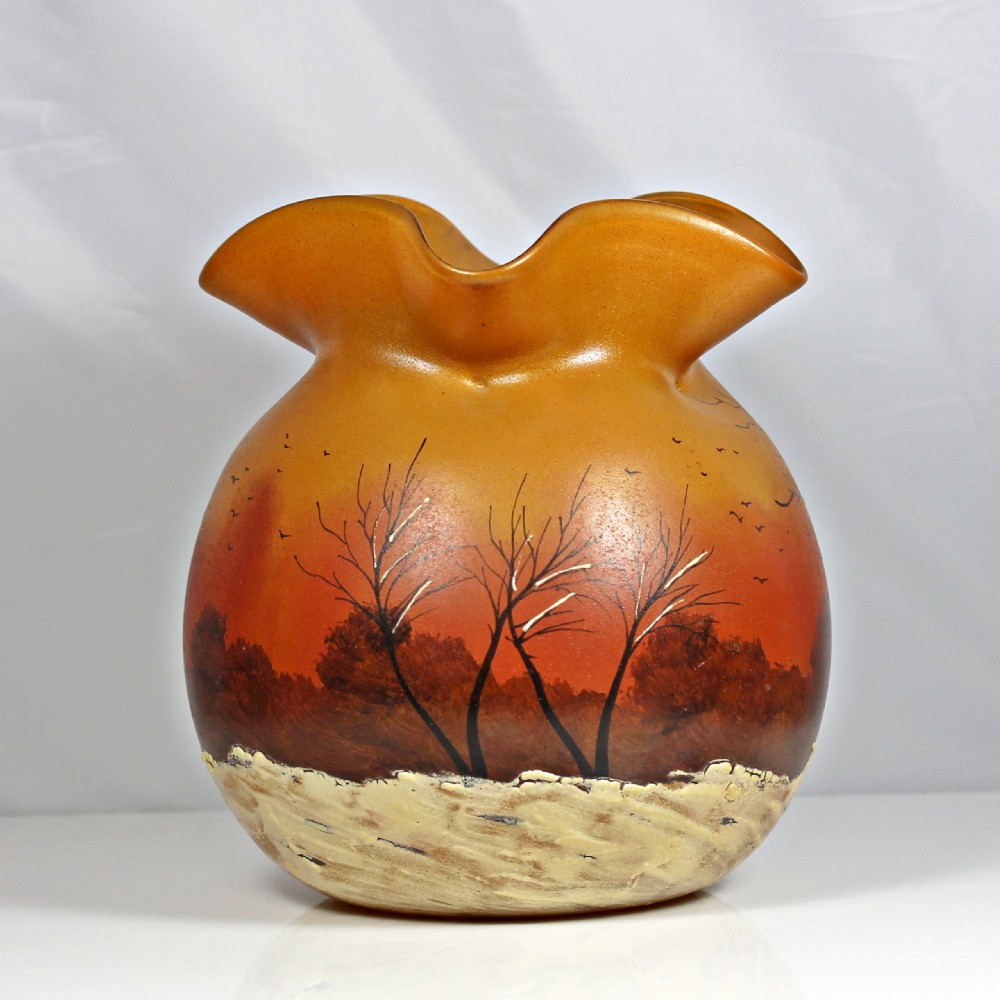 A globular Art Nouveau glass vase featuring an amber to orange gradient body, a ruffled rim, and a painted winter landscape with bare trees and textured white snow along the base.
