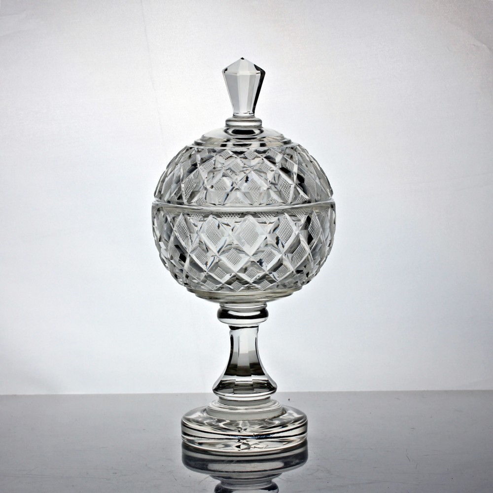An Edwardian clear cut glass lidded bowl featuring diamond facets, a pedestal stem, and a faceted top finial.
