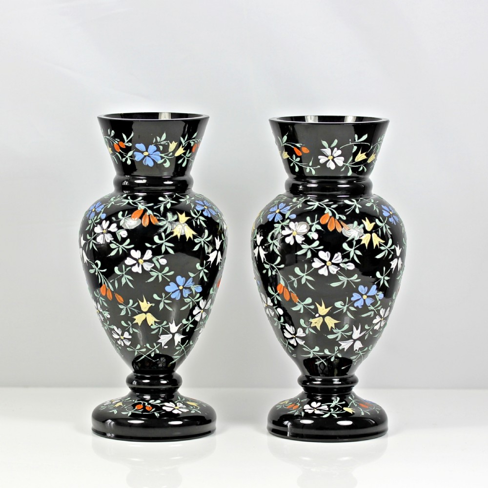 A pair of Victorian black glass vases featuring hand-painted floral enamel motifs in white, blue, yellow, and orange.