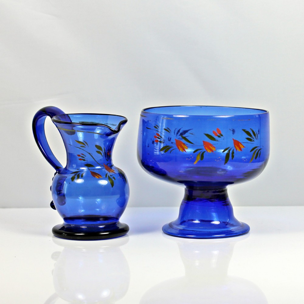 A hand-painted Bristol blue glass cream jug and matching pedestal sugar bowl decorated with floral motifs.