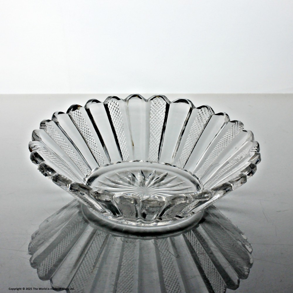 A clear cut glass preserve pot with a fitted lid and knopped finial resting on a matching scalloped glass saucer base. View VI