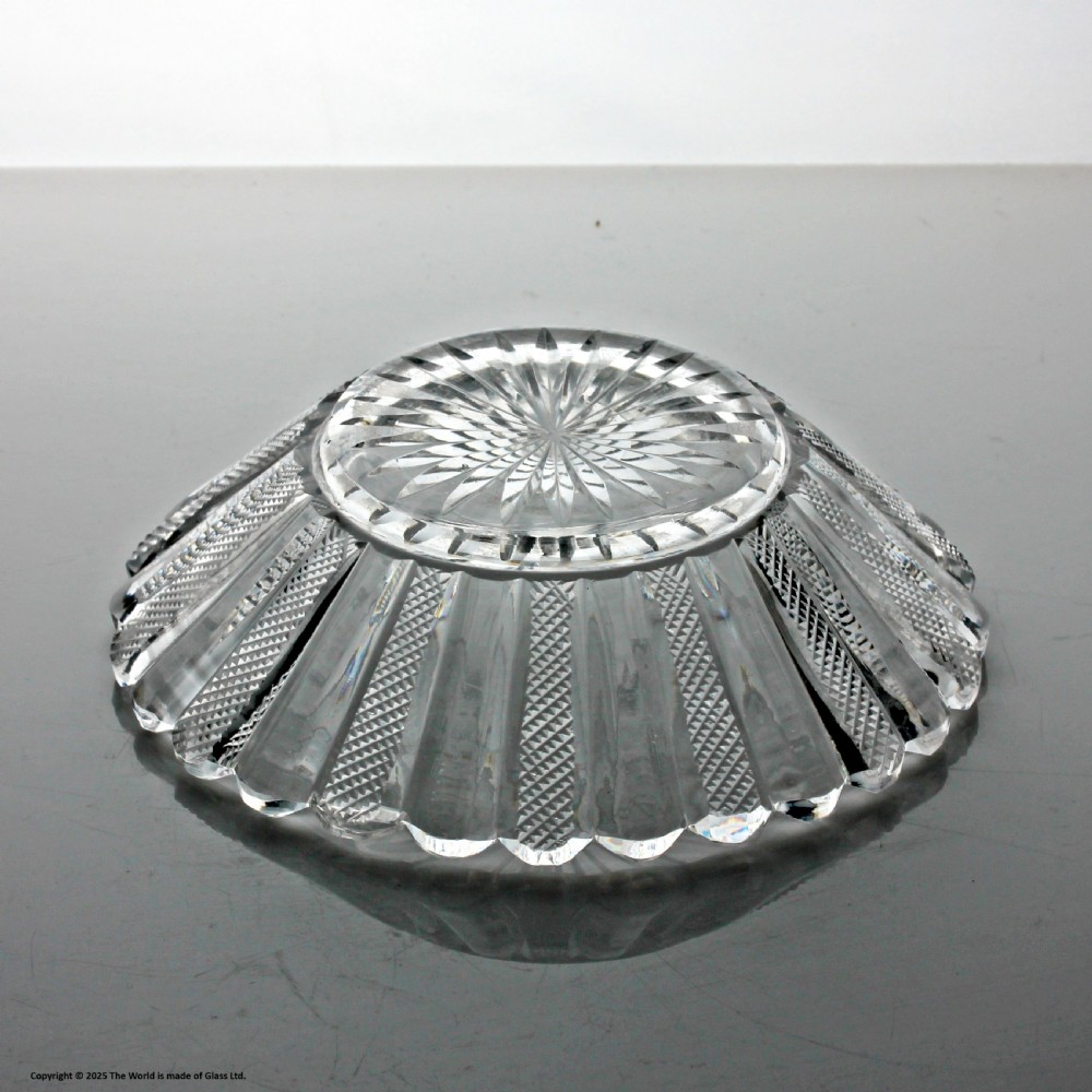 A clear cut glass preserve pot with a fitted lid and knopped finial resting on a matching scalloped glass saucer base. View VII