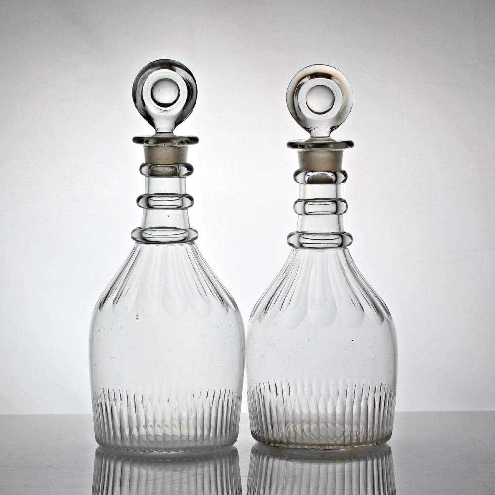 A pair of Georgian clear cut-glass decanters featuring three applied neck rings, fluted shoulders, vertical base cuts, and matching target stoppers.
