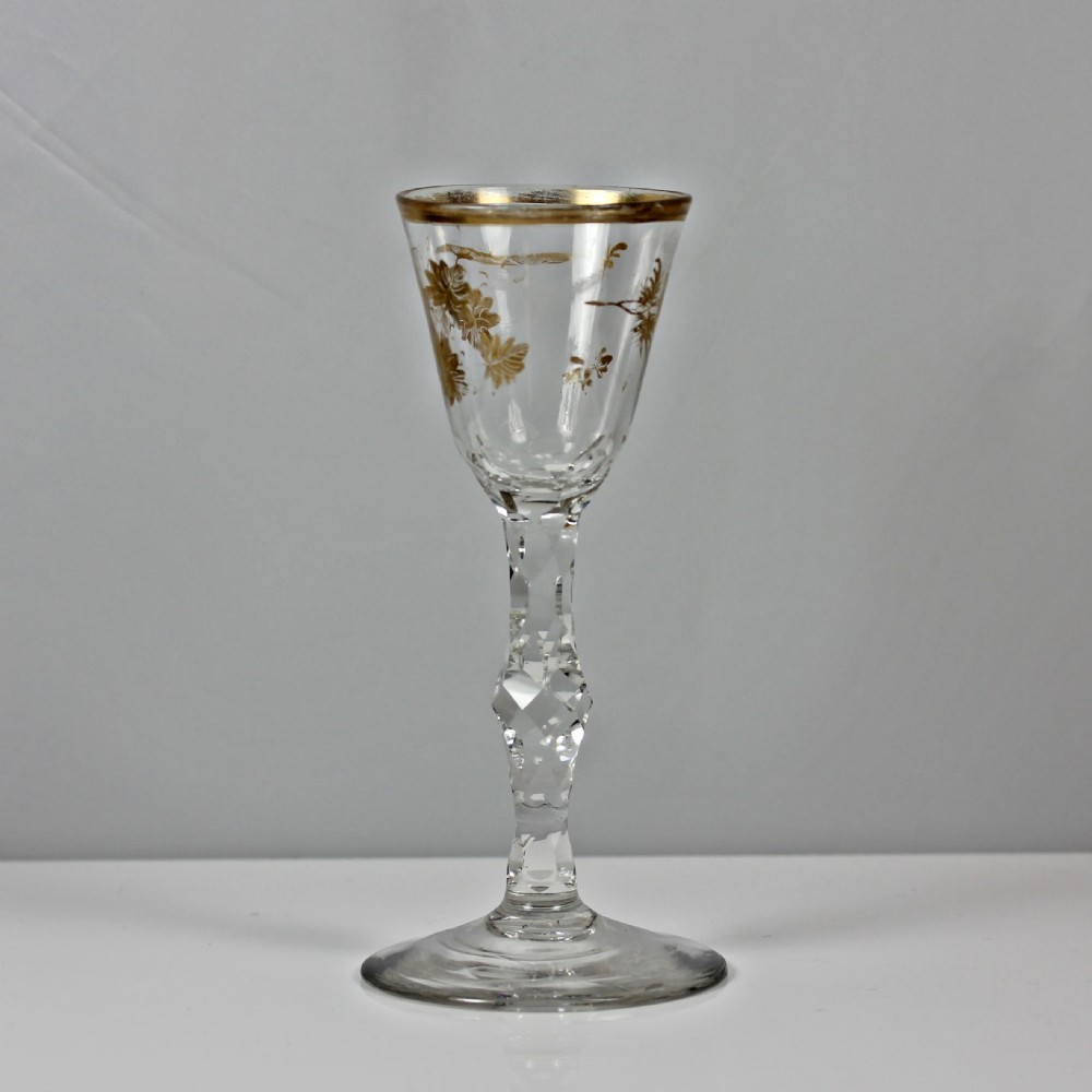 An 18th-century clear lead glass wine glass featuring a gilded vine leaf motif on the bowl and a geometric facet cut stem. View II