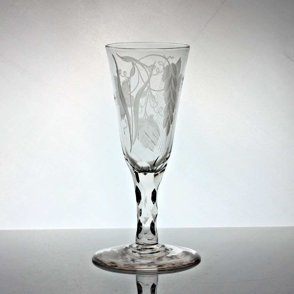 A tall Georgian clear glass ale flute featuring engraved hop and barley motifs on the bowl and a hexagonal facet-cut stem. View III