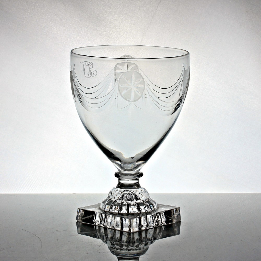 An antique Georgian clear glass rummer featuring an engraved ovoid bowl with swags and shield motifs resting on a square lemon squeezer base. View III