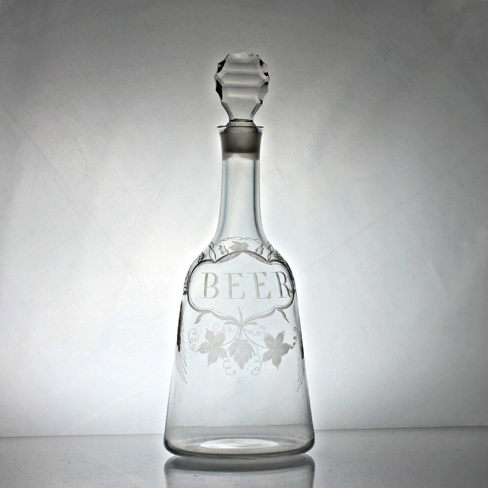A clear Georgian sugarloaf glass decanter featuring wheel-engraved foliage, a cartouche inscribed with the word BEER, and a faceted stopper.
