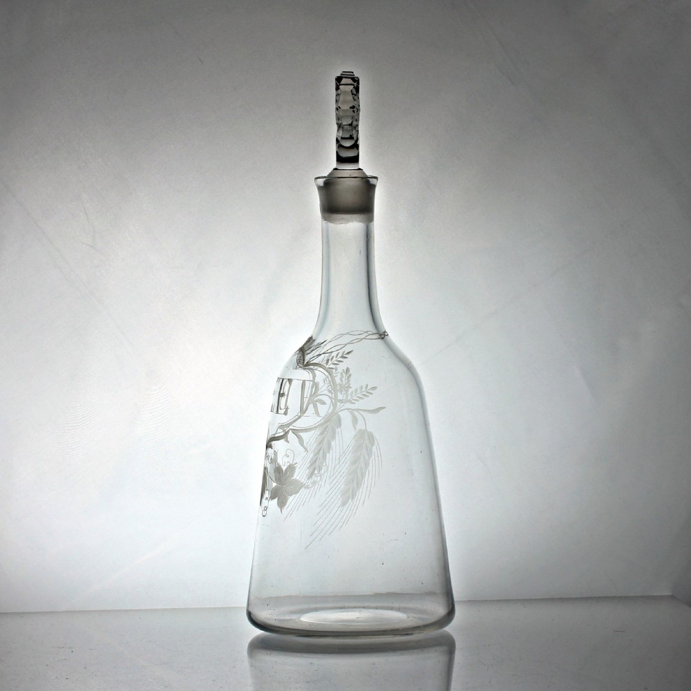 A clear Georgian sugarloaf glass decanter featuring wheel-engraved foliage, a cartouche inscribed with the word BEER, and a faceted stopper. View II
