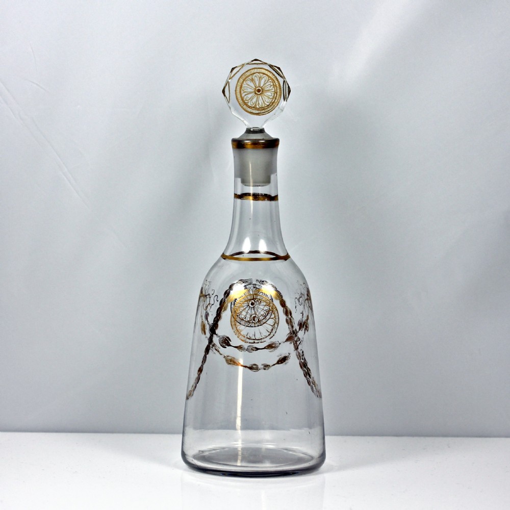An eighteenth-century clear glass decanter featuring gilded festoon patterns, gold rim details, and a faceted wheel-engraved stopper with gilt rosettes.