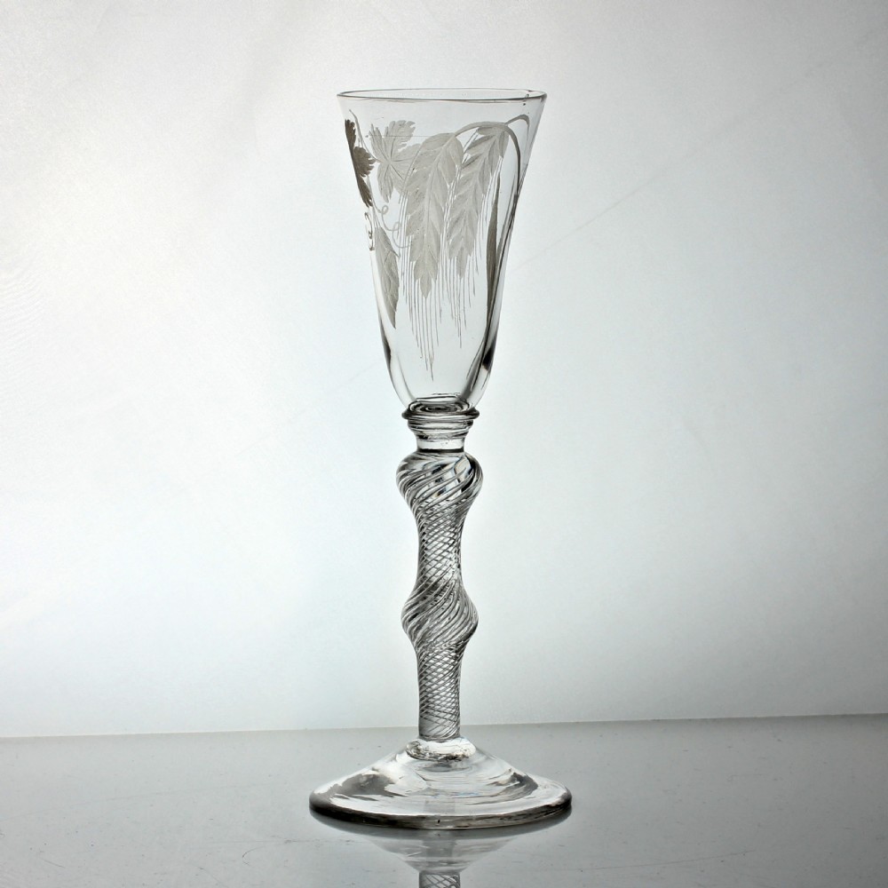 A tall clear glass ale flute with wheel-engraved hop and barley motifs above a knopped multi-spiral air twist stem and conical foot. View III