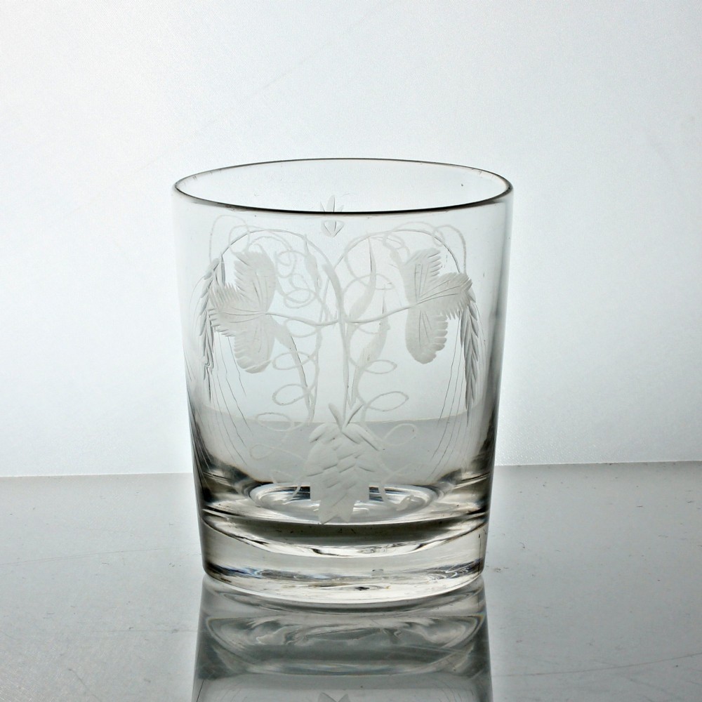 A clear Georgian glass tumbler featuring wheel-engraved motifs of hops and barley around its cylindrical body.