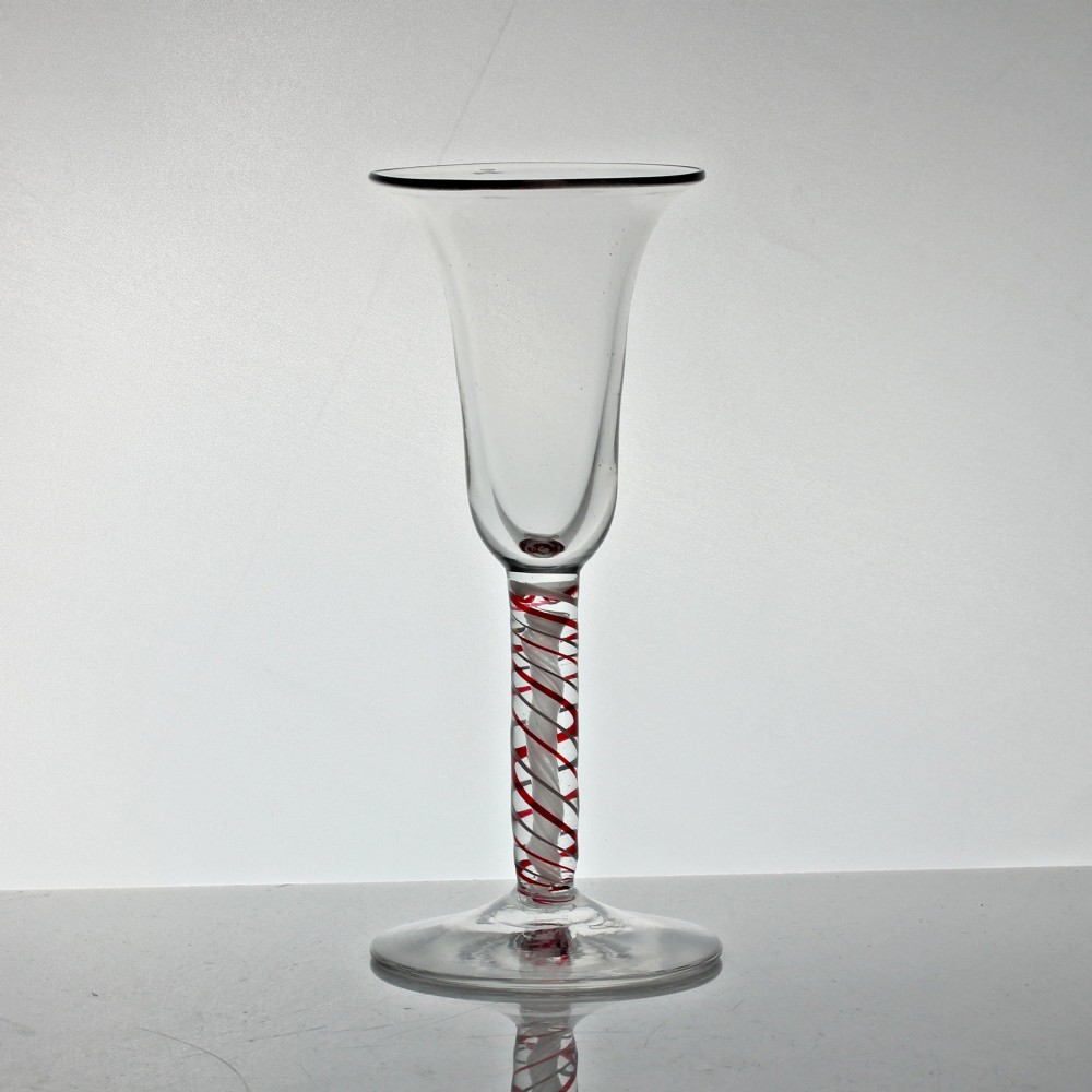 A hand-blown clear glass wine goblet featuring a flared bowl and a stem containing a red and white spiral twist above a circular flat base.
