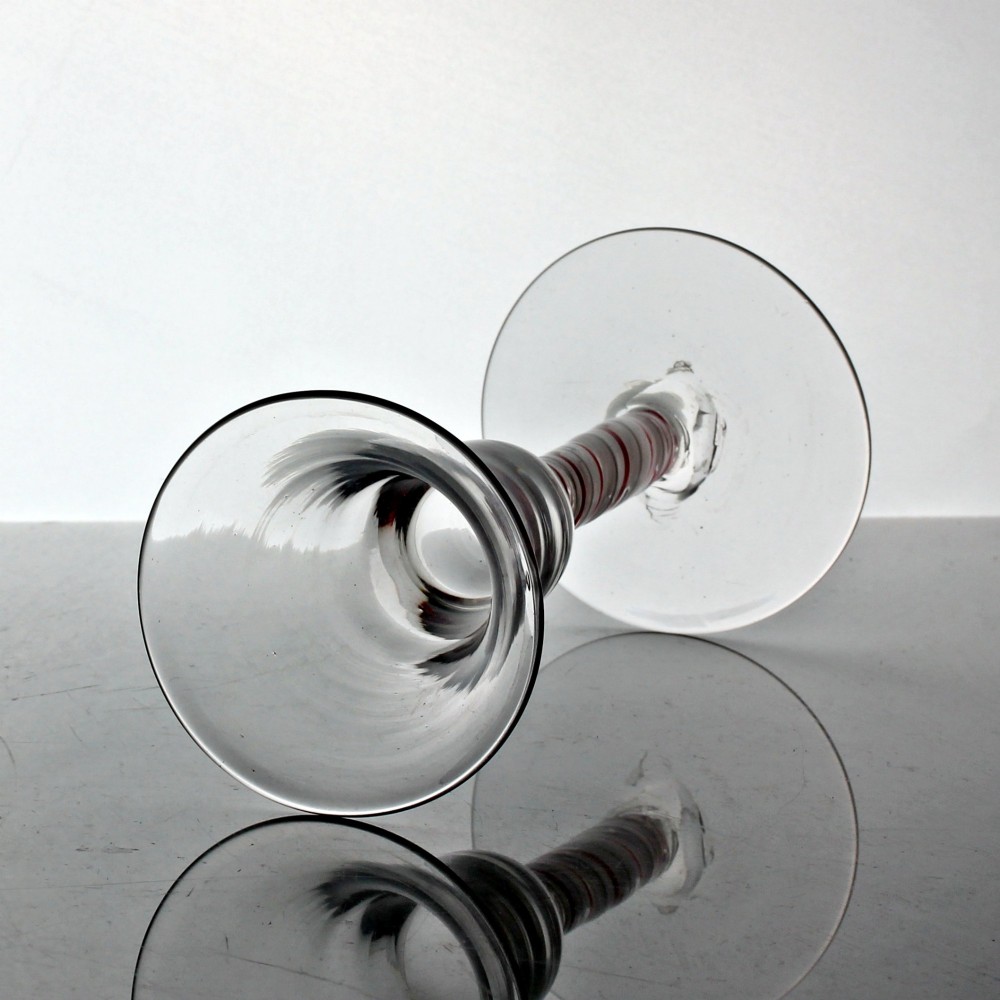 A hand-blown clear glass wine goblet featuring a flared bowl and a stem containing a red and white spiral twist above a circular flat base. View II