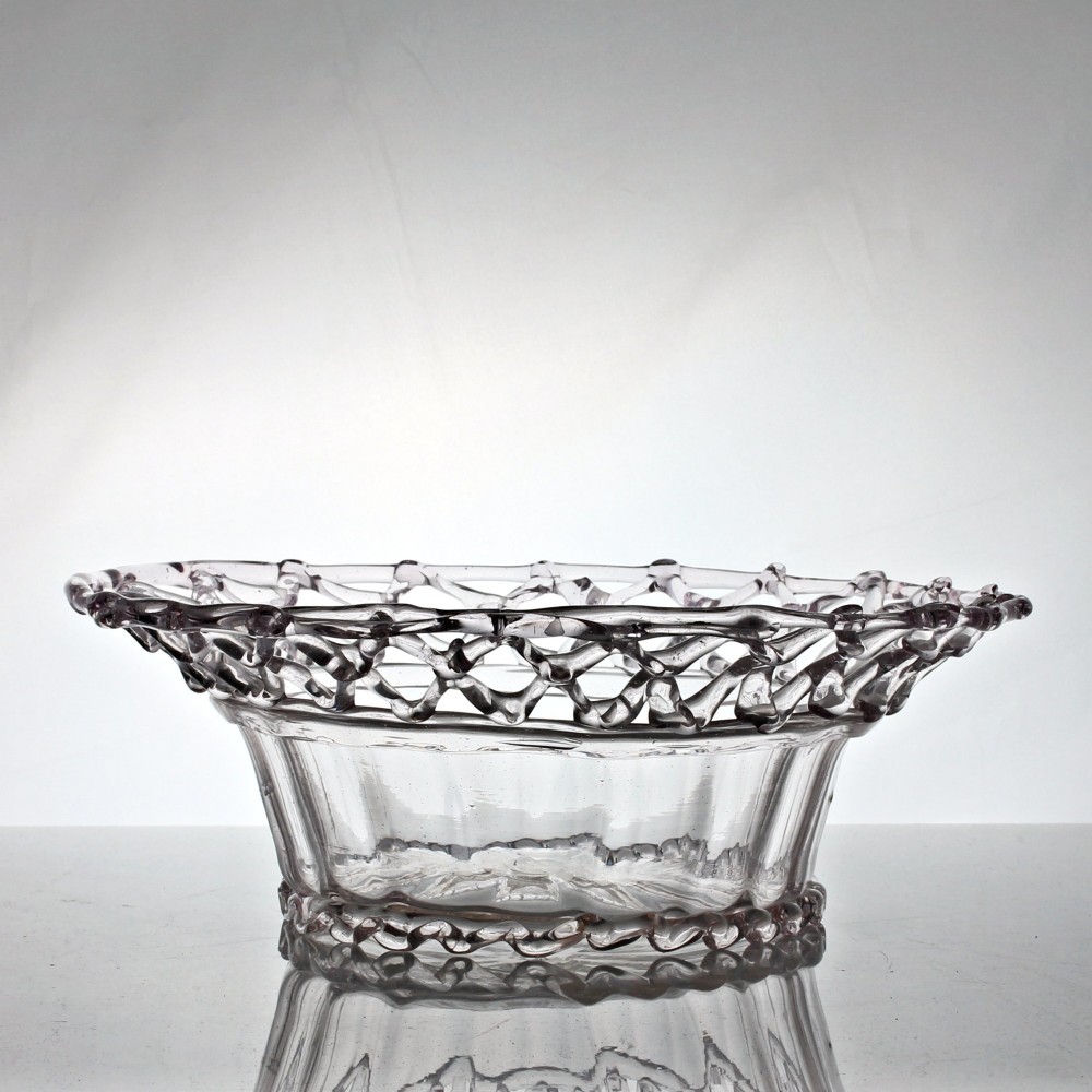 A clear hand-blown glass bowl featuring a fluted lower body and an openwork reticulated lattice rim.