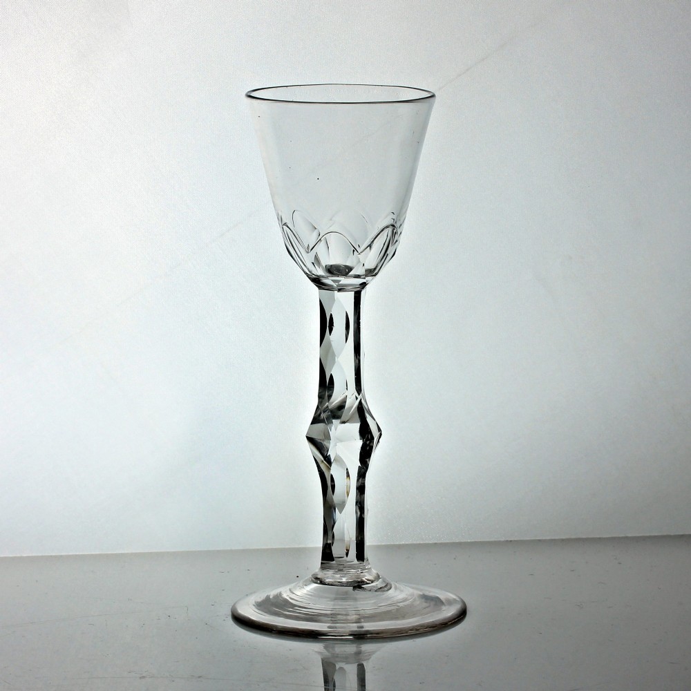 A Georgian clear glass wine goblet featuring a conical bowl, a facet-cut knopped stem, and a circular flat foot.