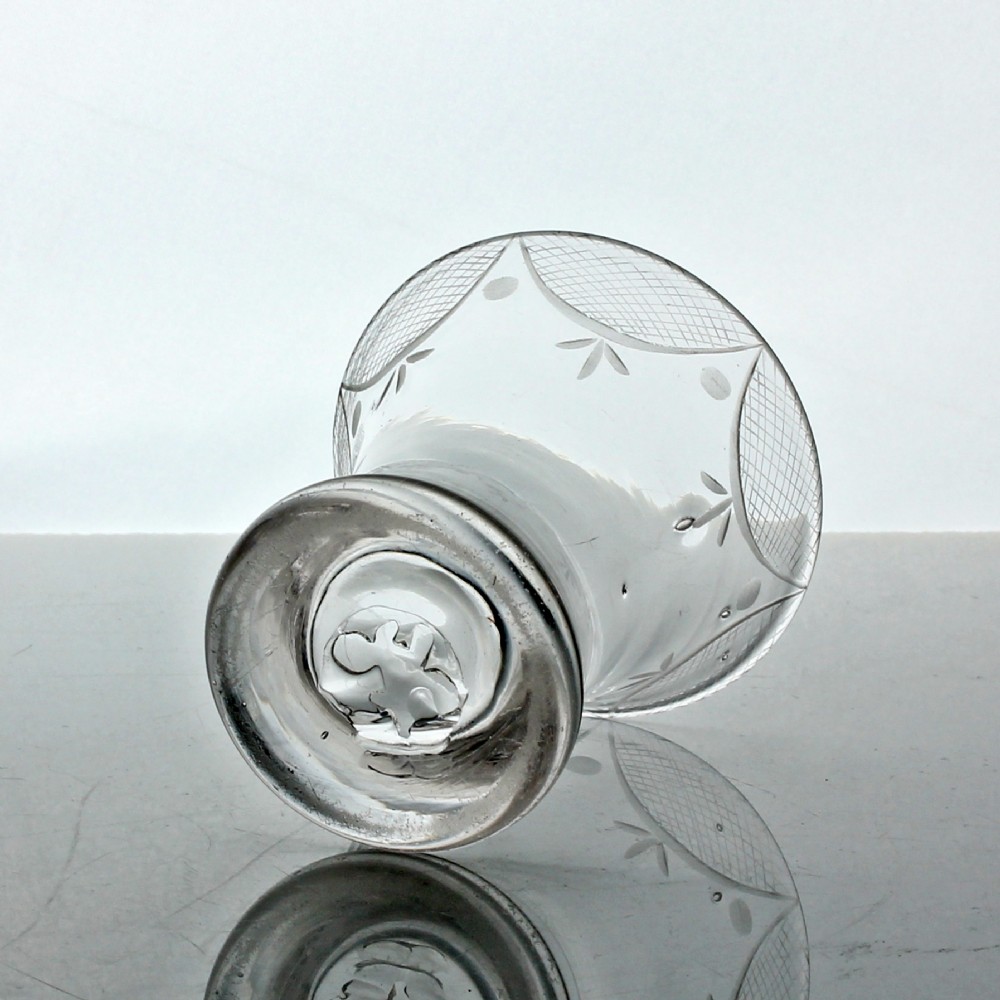 A small clear Georgian firing glass featuring a flared rim, heavy circular base, and wheel-engraved swag and tail decoration. View III