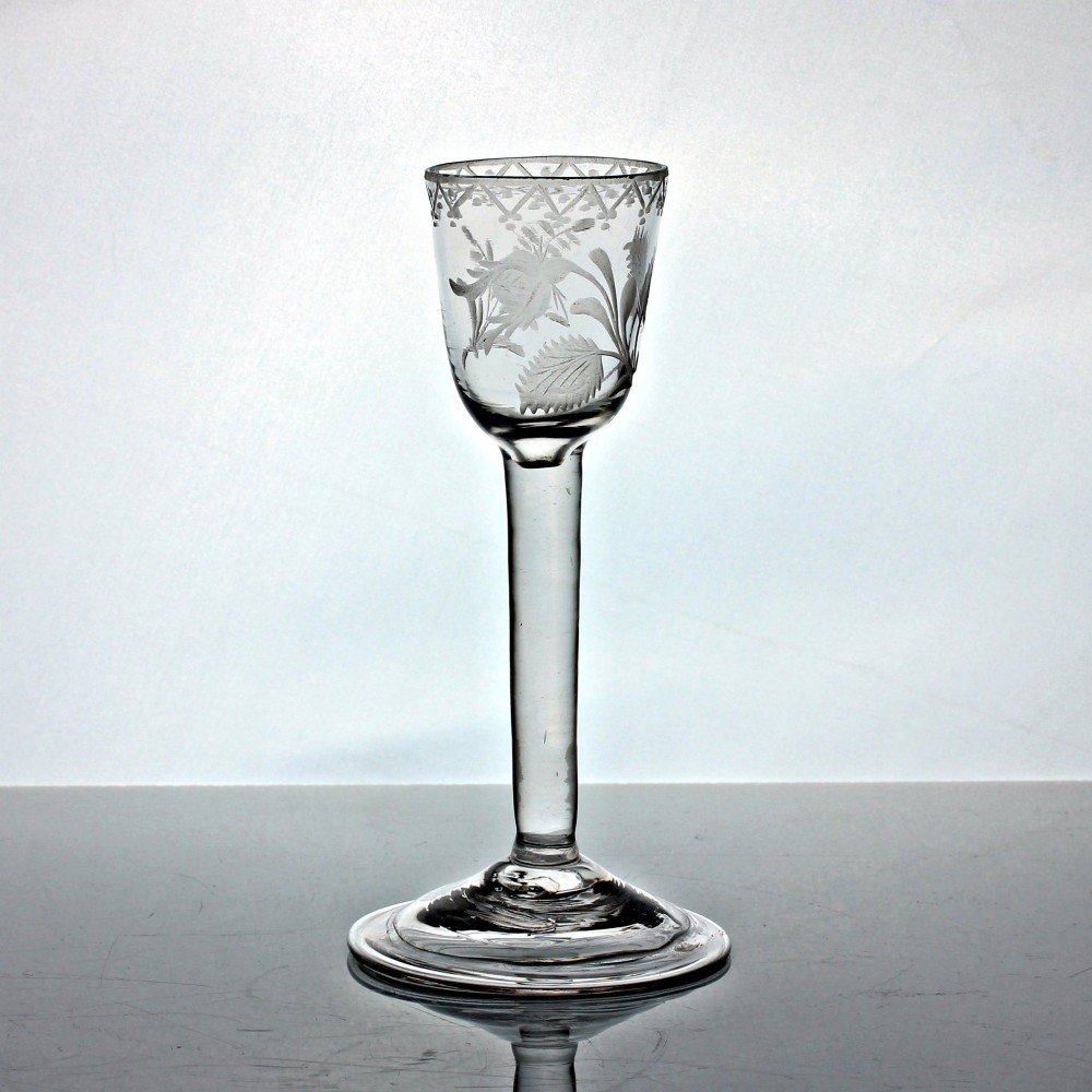 An 18th-century Georgian clear lead glass wine glass featuring a plain stem, circular base, and wheel-engraved floral motif on the bowl.