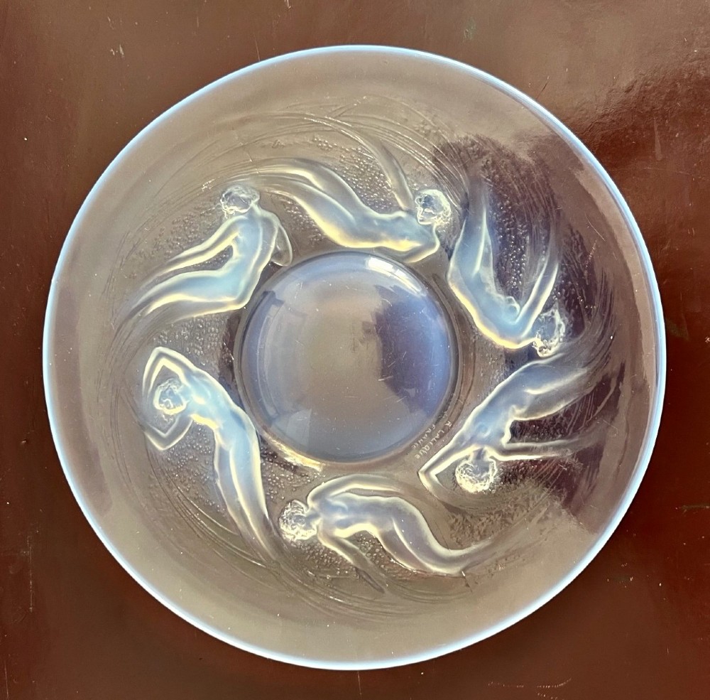 A circular Rene Lalique opalescent glass dish featuring a relief pattern of six swirling female nudes surrounding a smooth central recess.