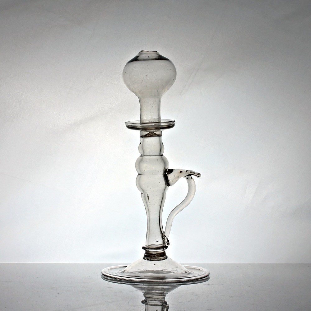 A tall Georgian hand-blown clear glass oil lamp featuring a bulbous top reservoir, a knopped central stem with an applied loop handle, and a wide circular foot.