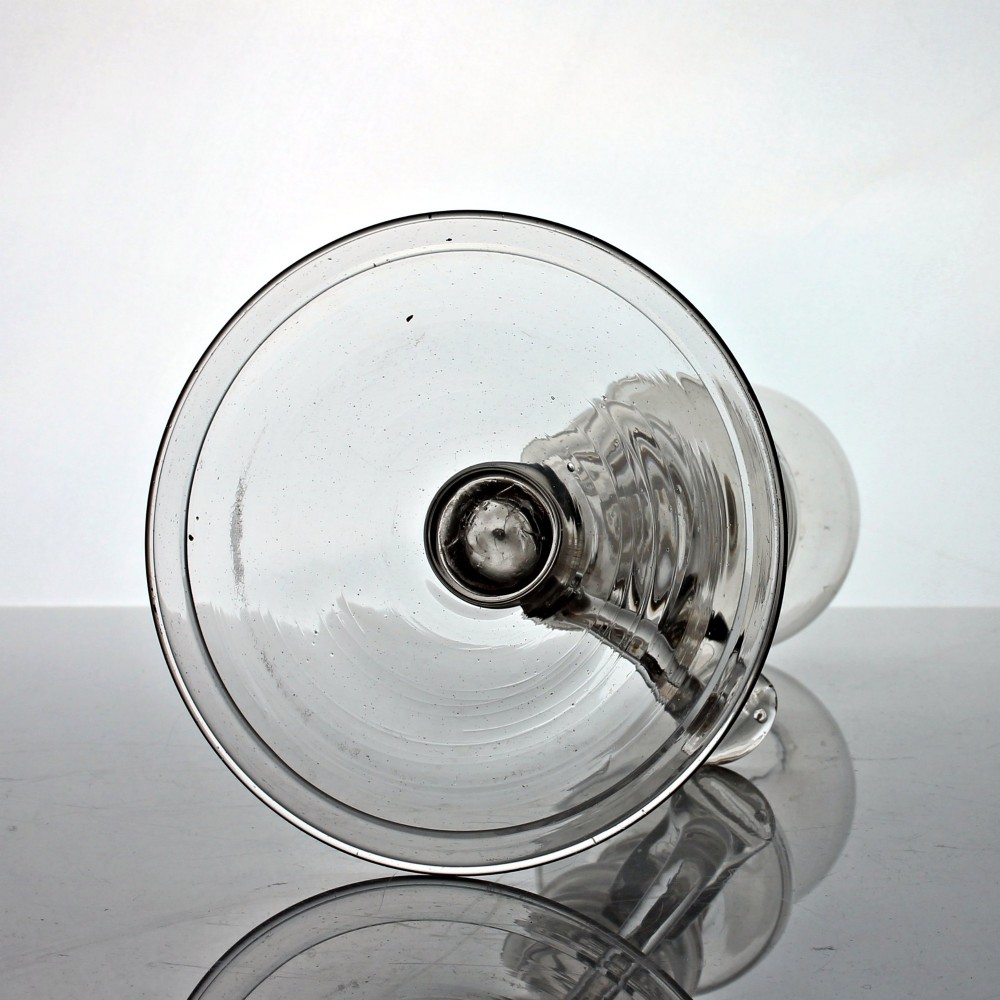 A tall Georgian hand-blown clear glass oil lamp featuring a bulbous top reservoir, a knopped central stem with an applied loop handle, and a wide circular foot. View V