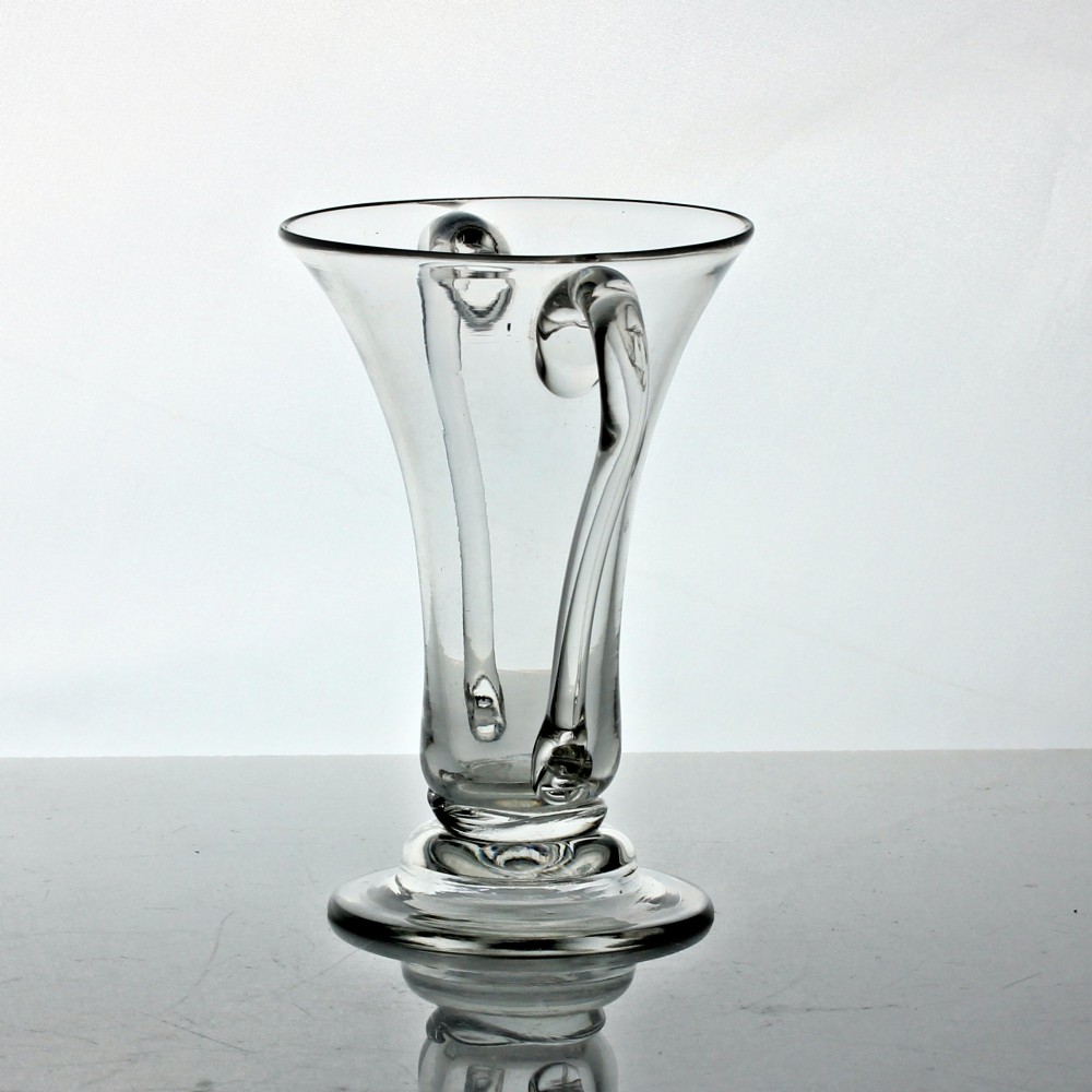 A clear Georgian hand-blown glass cup featuring two curved side handles, a flared rim, and a thick pedestal base. View II