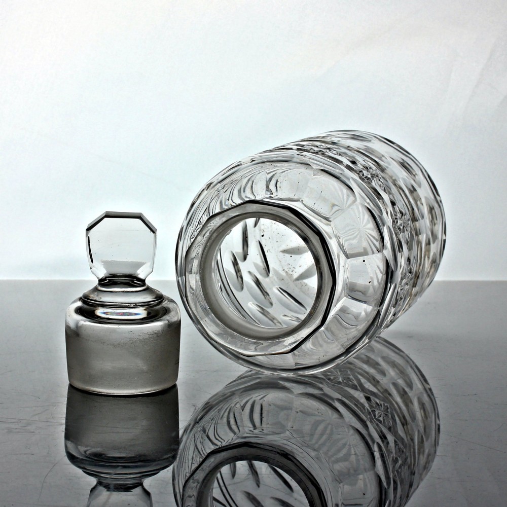 An early Victorian clear cut glass cylindrical pickle jar featuring geometric starburst cuts, round printie cuts, and a faceted glass stopper lid. View II
