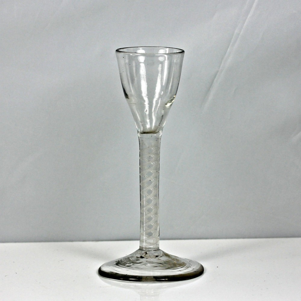 An antique clear glass wine glass featuring a bell-shaped bowl, an internal white opaque twist stem, and a flat conical base.