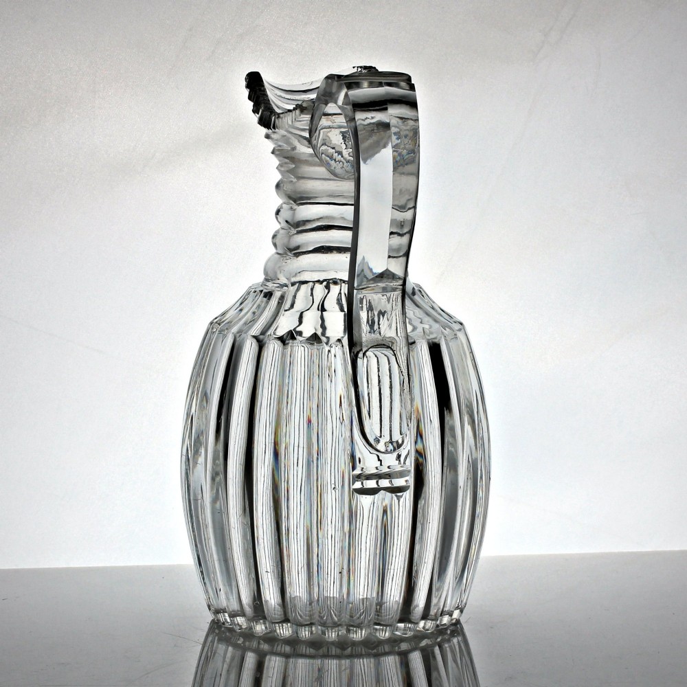 A clear Georgian lead crystal water jug featuring vertical pillar cutting around the lower body, neck rings, and a notched poured spout with an applied handle. View II