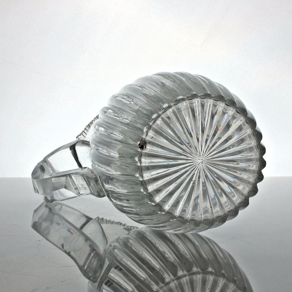 A clear Georgian lead crystal water jug featuring vertical pillar cutting around the lower body, neck rings, and a notched poured spout with an applied handle. View IV
