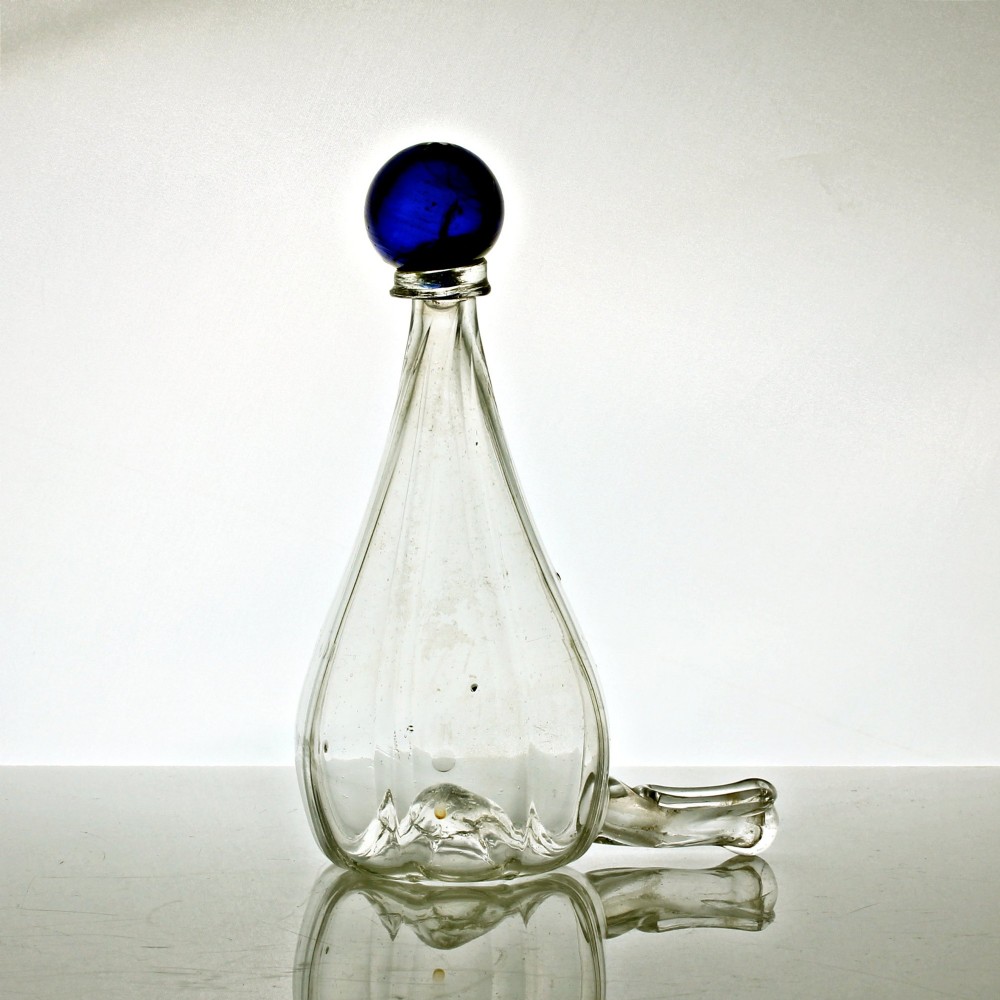 A clear ribbed glass conical bird feeder featuring an attached side drinking spout and topped with a solid cobalt blue glass spherical finial.