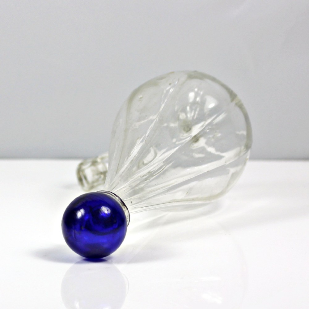A clear ribbed glass conical bird feeder featuring an attached side drinking spout and topped with a solid cobalt blue glass spherical finial. View IV
