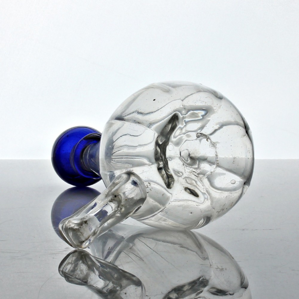 A clear ribbed glass conical bird feeder featuring an attached side drinking spout and topped with a solid cobalt blue glass spherical finial. View V