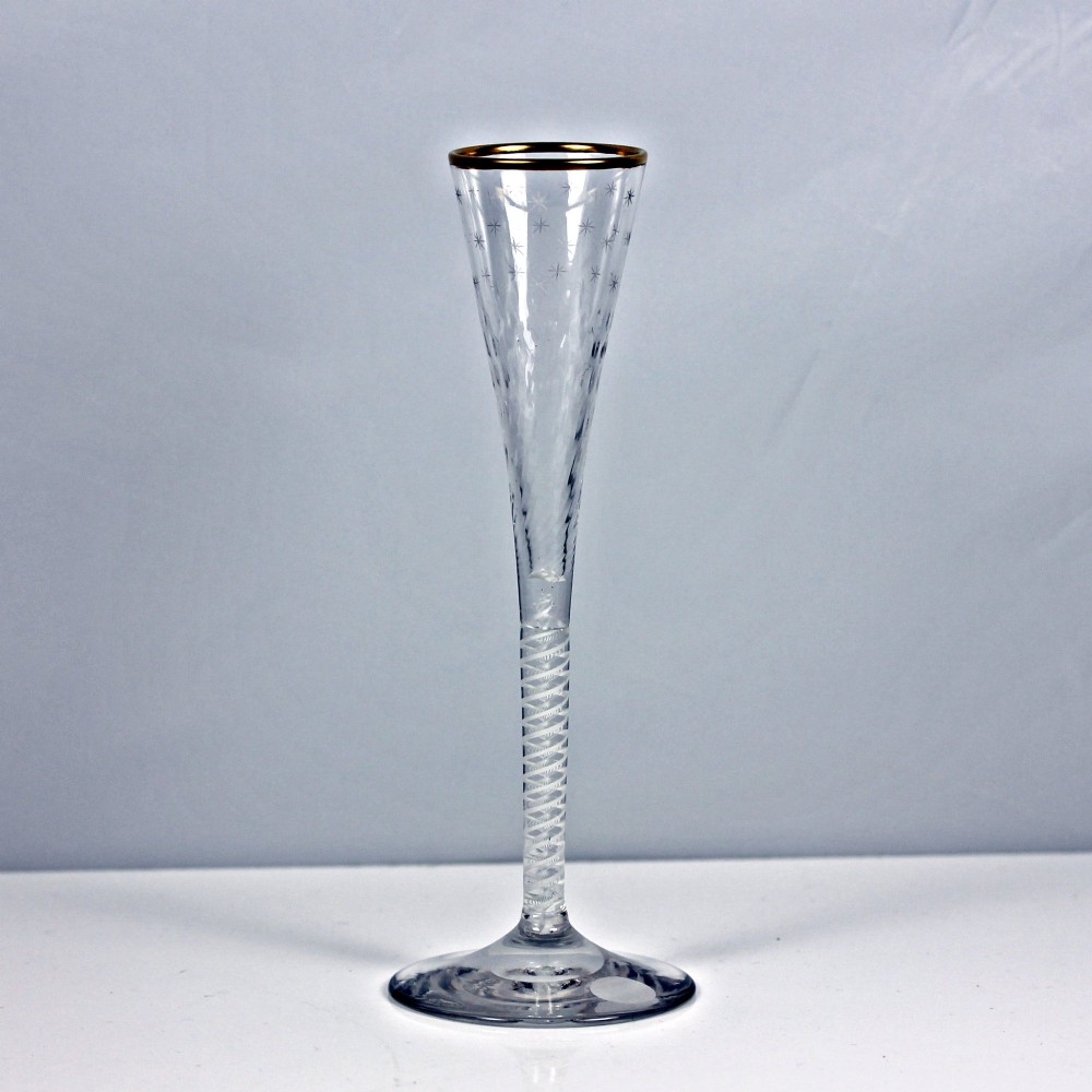 A tall Georgian clear lead glass ratafia flute featuring an engraved star pattern, gilded rim, white double series opaque twist stem, and a flat circular foot.