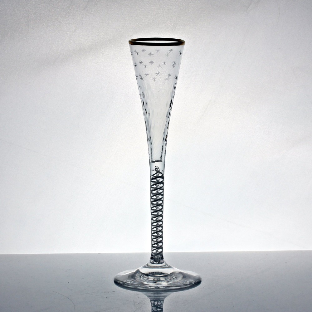 A tall Georgian clear lead glass ratafia flute featuring an engraved star pattern, gilded rim, white double series opaque twist stem, and a flat circular foot. View II
