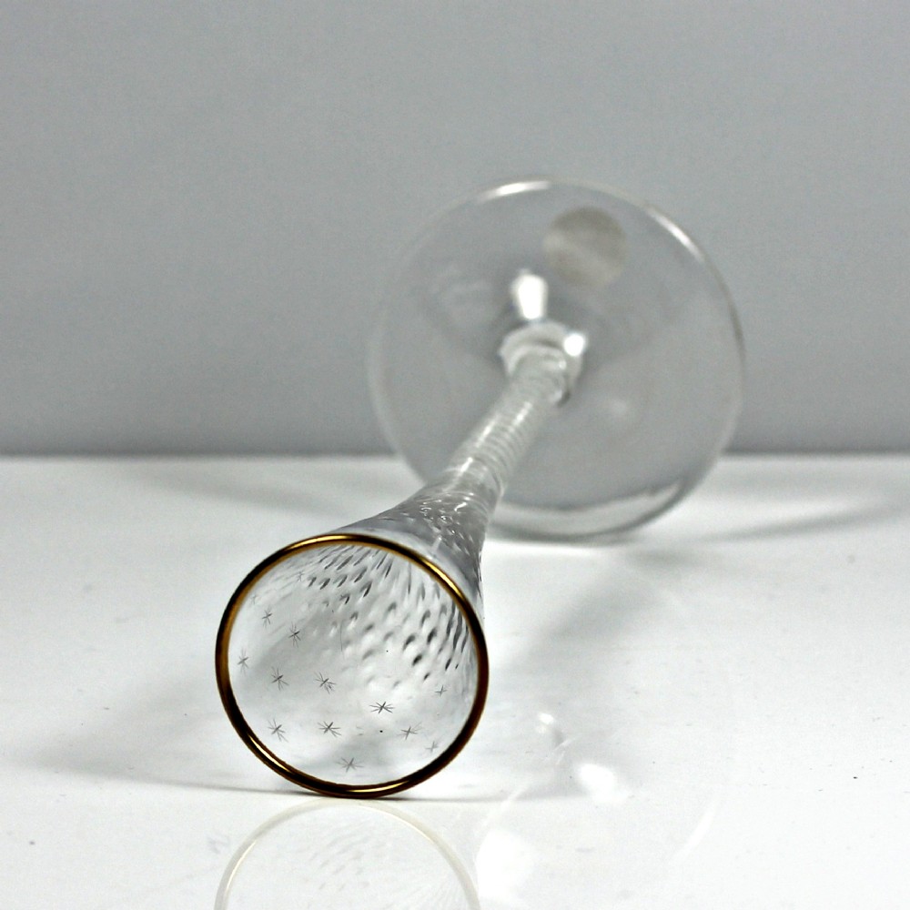 A tall Georgian clear lead glass ratafia flute featuring an engraved star pattern, gilded rim, white double series opaque twist stem, and a flat circular foot. View III