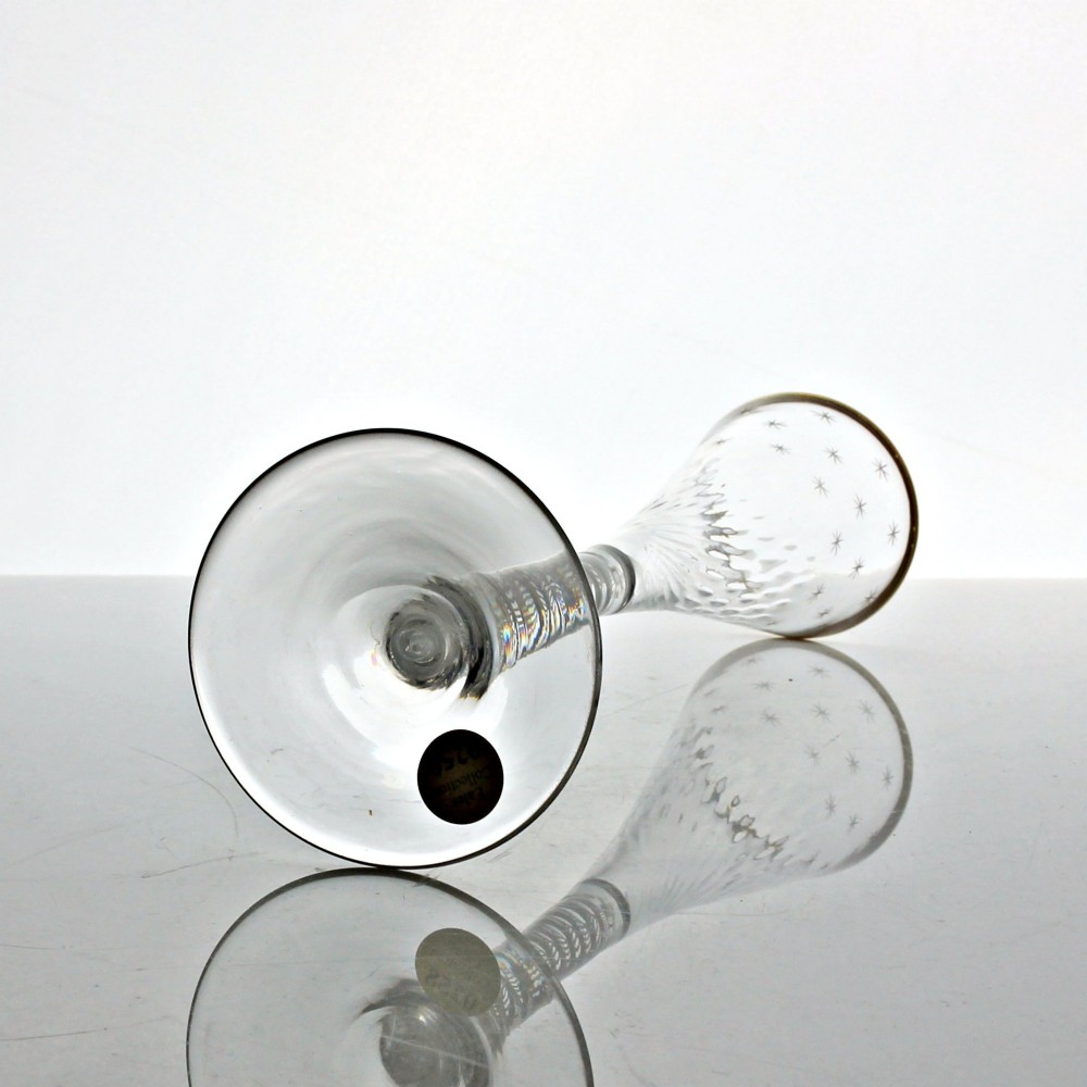 A tall Georgian clear lead glass ratafia flute featuring an engraved star pattern, gilded rim, white double series opaque twist stem, and a flat circular foot. View IV