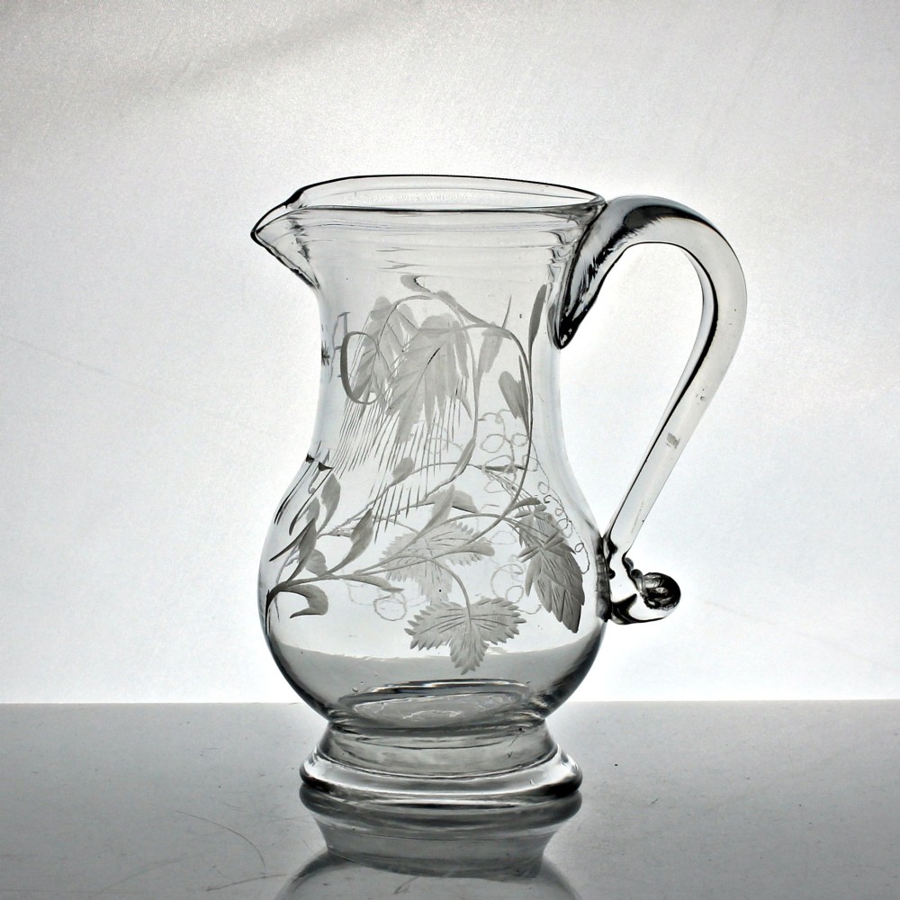 A clear glass Georgian jug decorated with wheel-engraved hop and barley motifs and fitted with an applied loop handle.