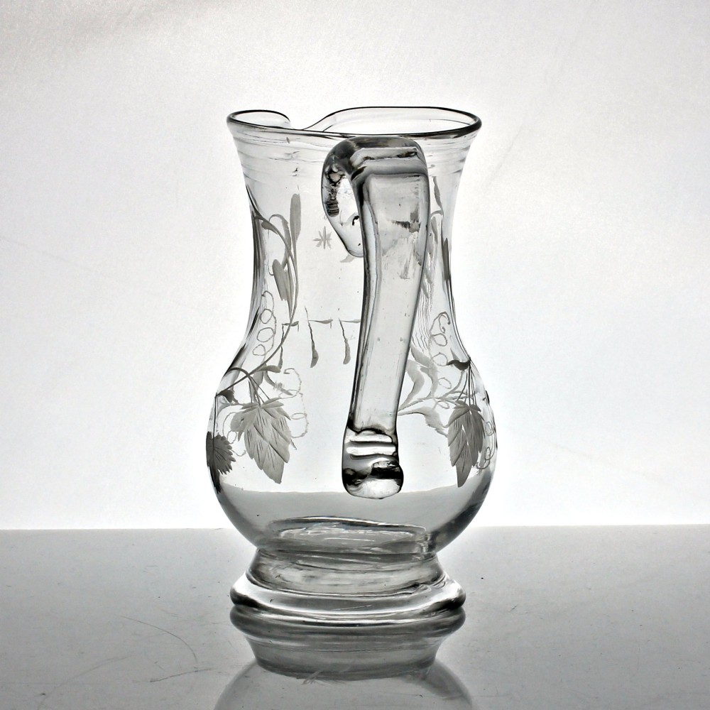 A clear glass Georgian jug decorated with wheel-engraved hop and barley motifs and fitted with an applied loop handle. View II